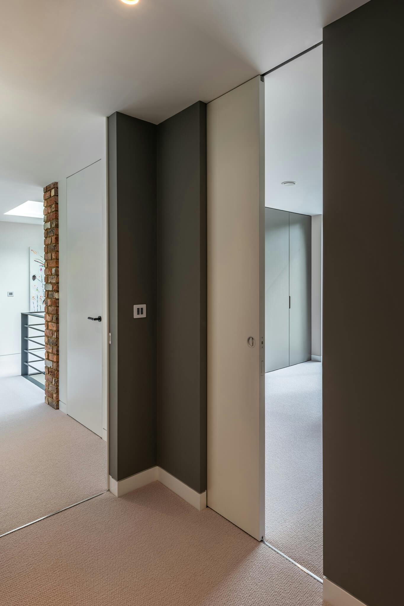 A contemporary upstairs reception area with a flush door and sliding door leading into a carpeted bedroom with dark grey walls.