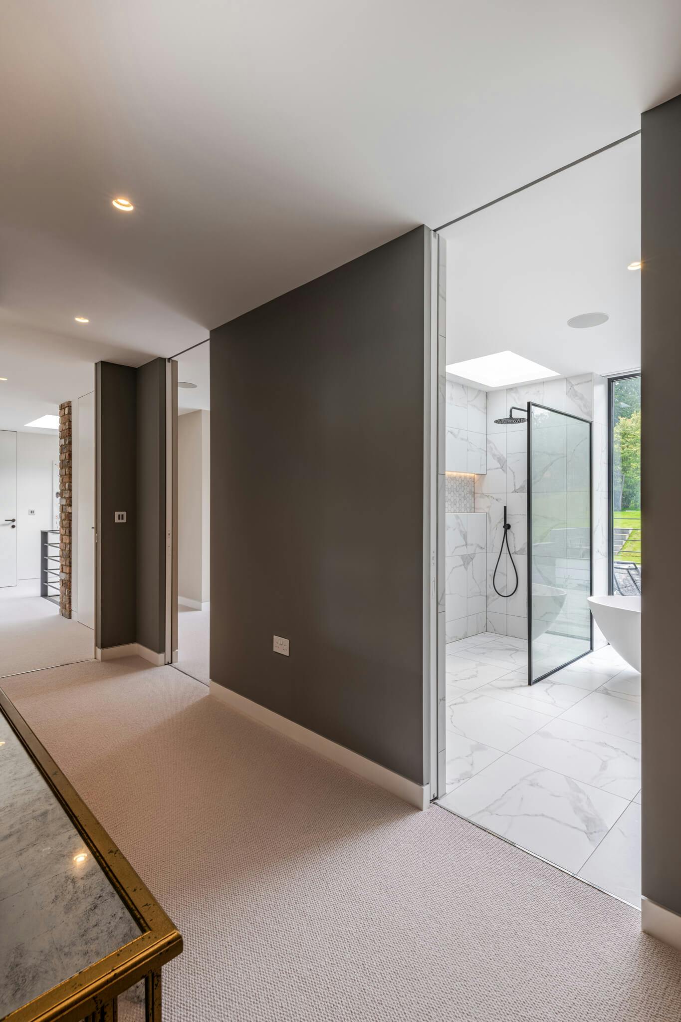 A carpeted hallway with dark grey walls and an opening leading to a white and black tiled bathroom.