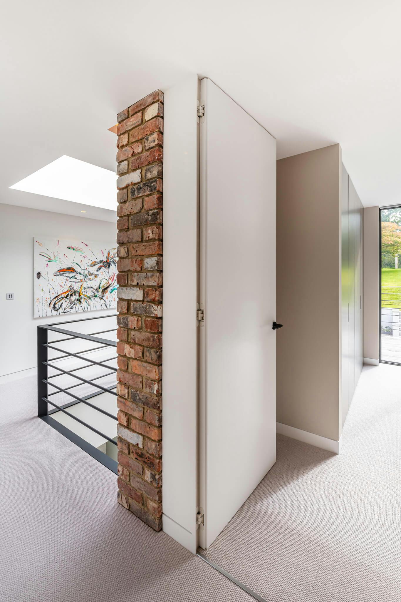 A carpeted upstairs landing with rooflight, brick wall feature and white fully open flush door leading into a bedroom.