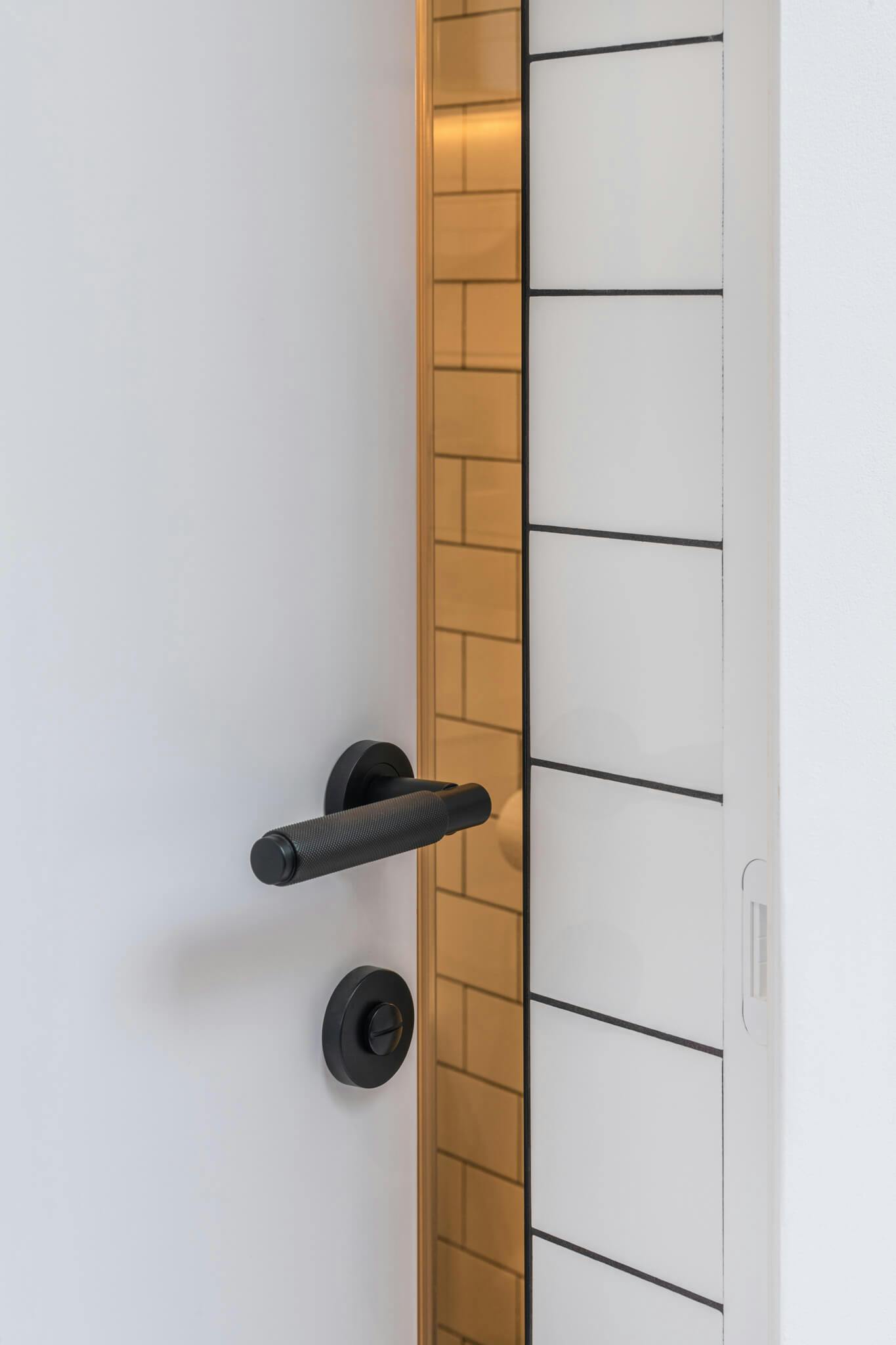 A white door slighly ajar leading into a tiled room, door with a black lever and privacy lock and white keep in the frame.