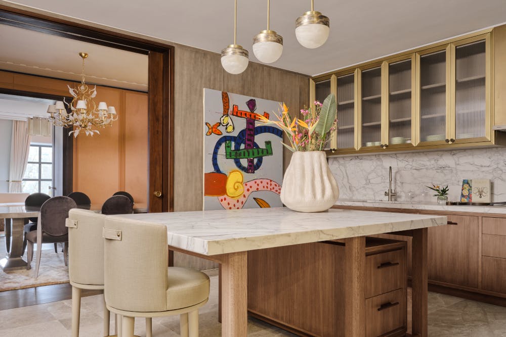 A contemporary luxury marble tiled kitchen with wooden cabinets, young abstract art on the wall and a large opening through to the dining area.