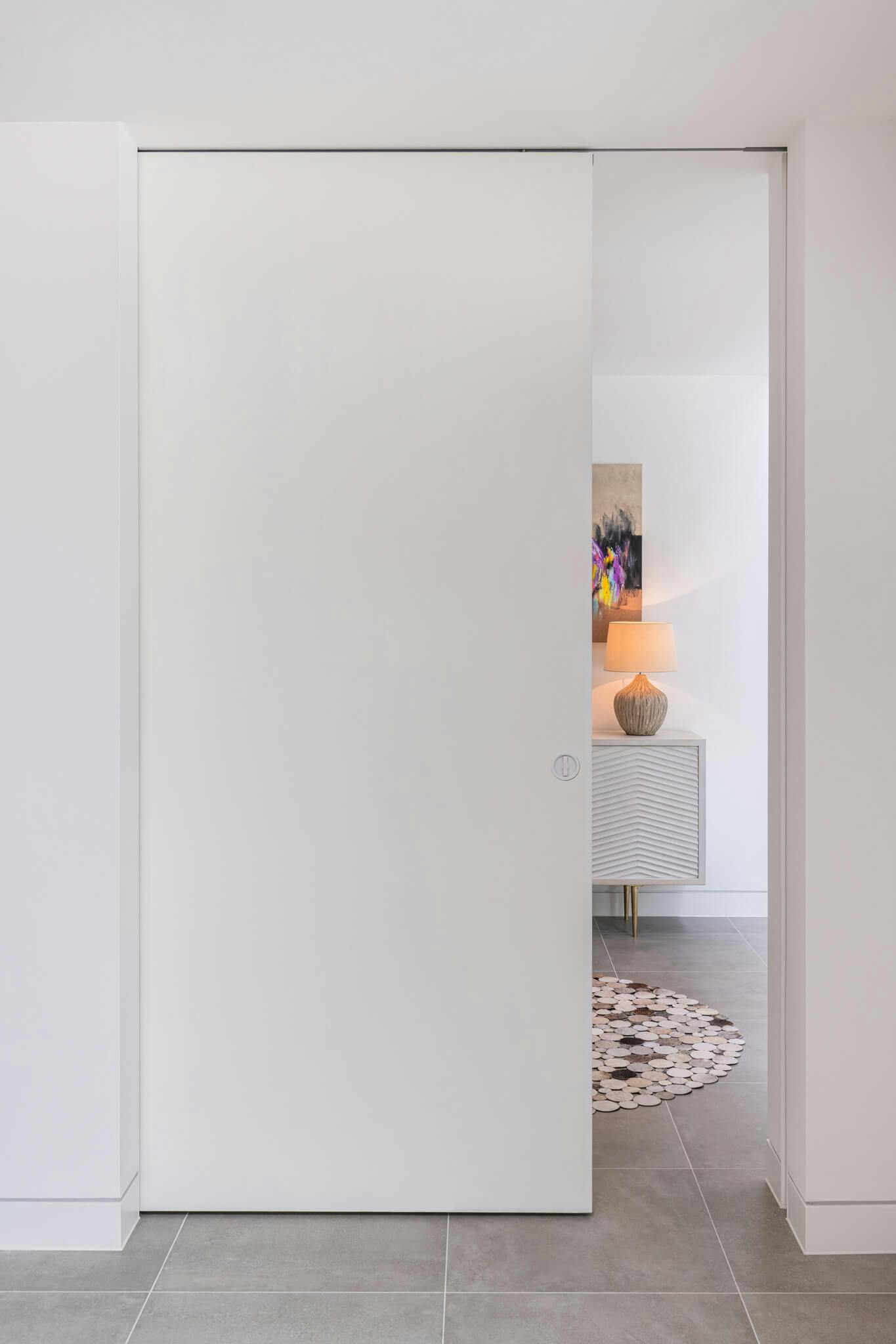 A white contemporary interior with a partially closed pocket sliding door leading to a reception area.