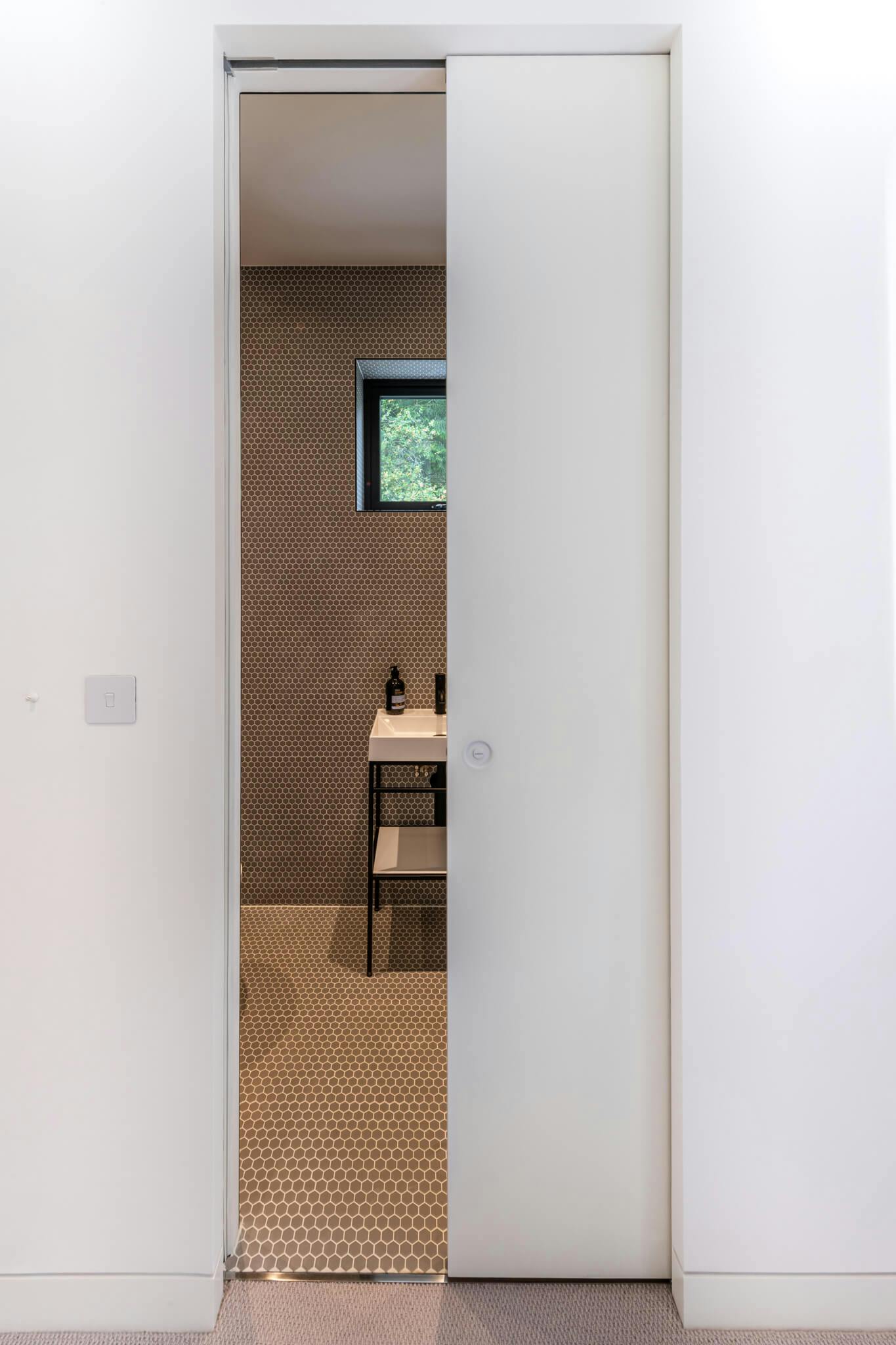 A white single sliding pocket door partially open leading to a tiled bathroom