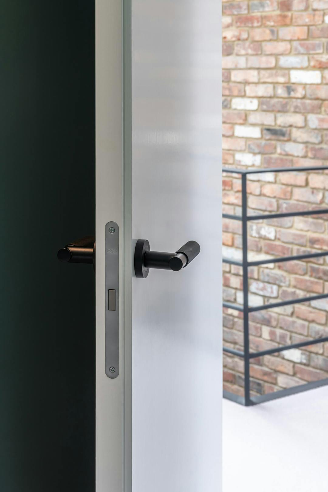 Looking at the side profile of an open door with a magnetic latch, black lever handles and in a brick feature wall and steel rail in the background.