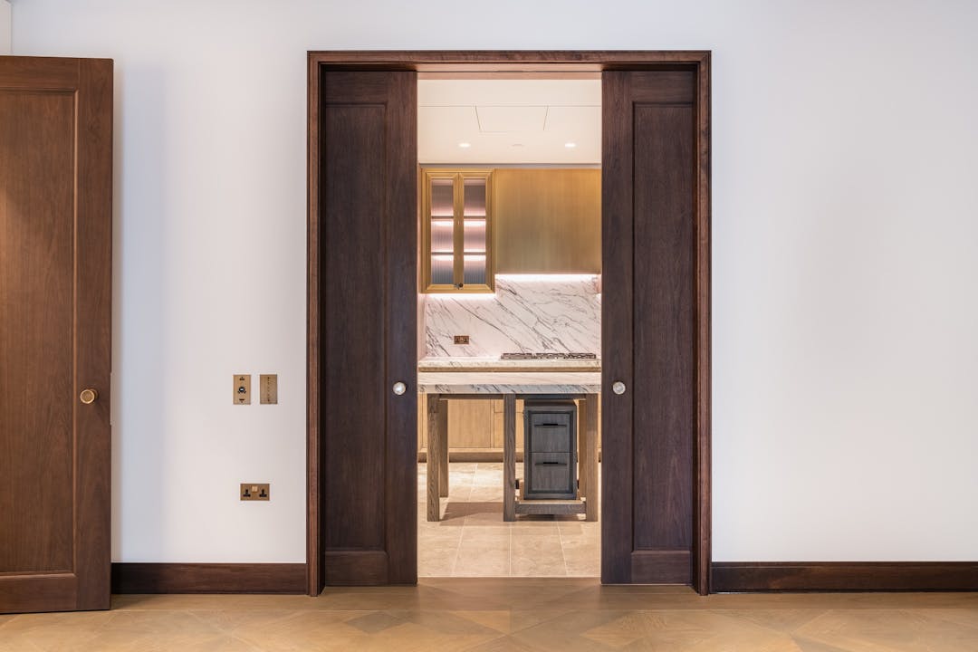 A set of large dark wood double pocket sliding doors leading through into a luxury marble kitchen.