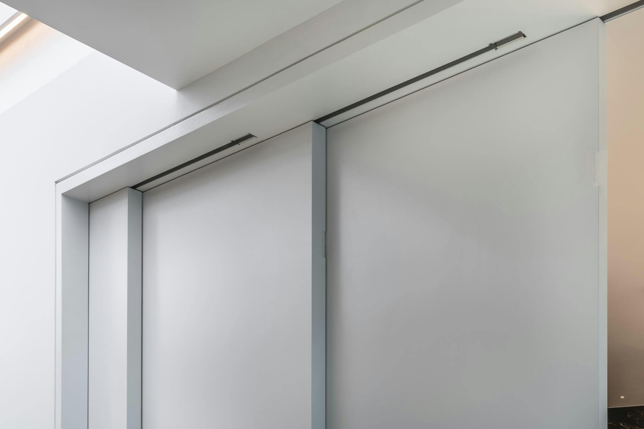 White telescopic sliding doors showing track detail that are slightly open showing the ceiling of the adjoining room.