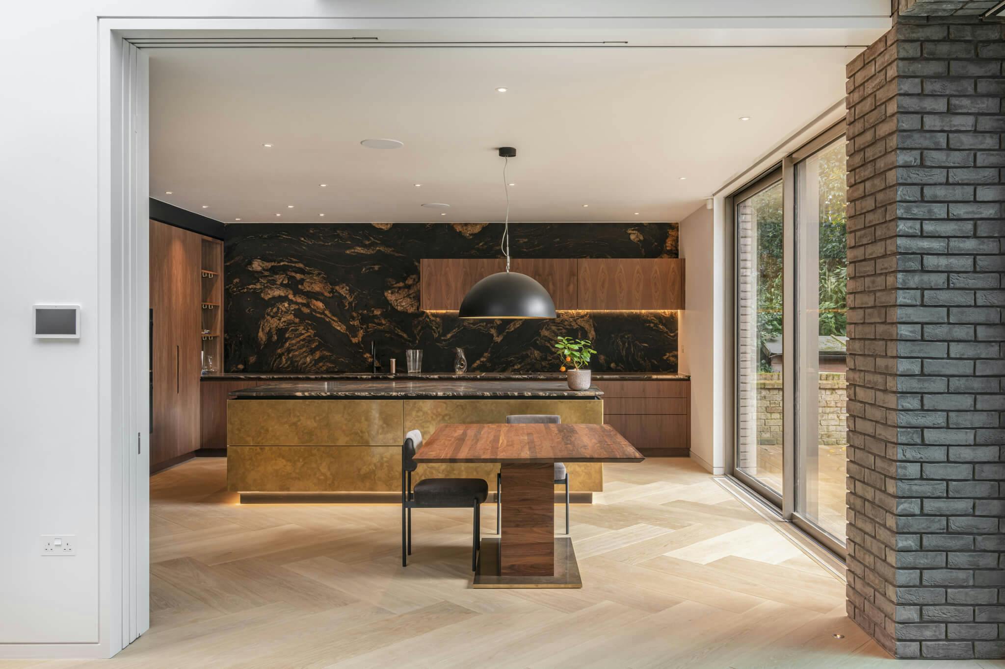 A fully open telescopic sliding door opening to a wooden floored brown marbled kitchen with a large metal dome light and exterior glazed sliding doors to the outside.