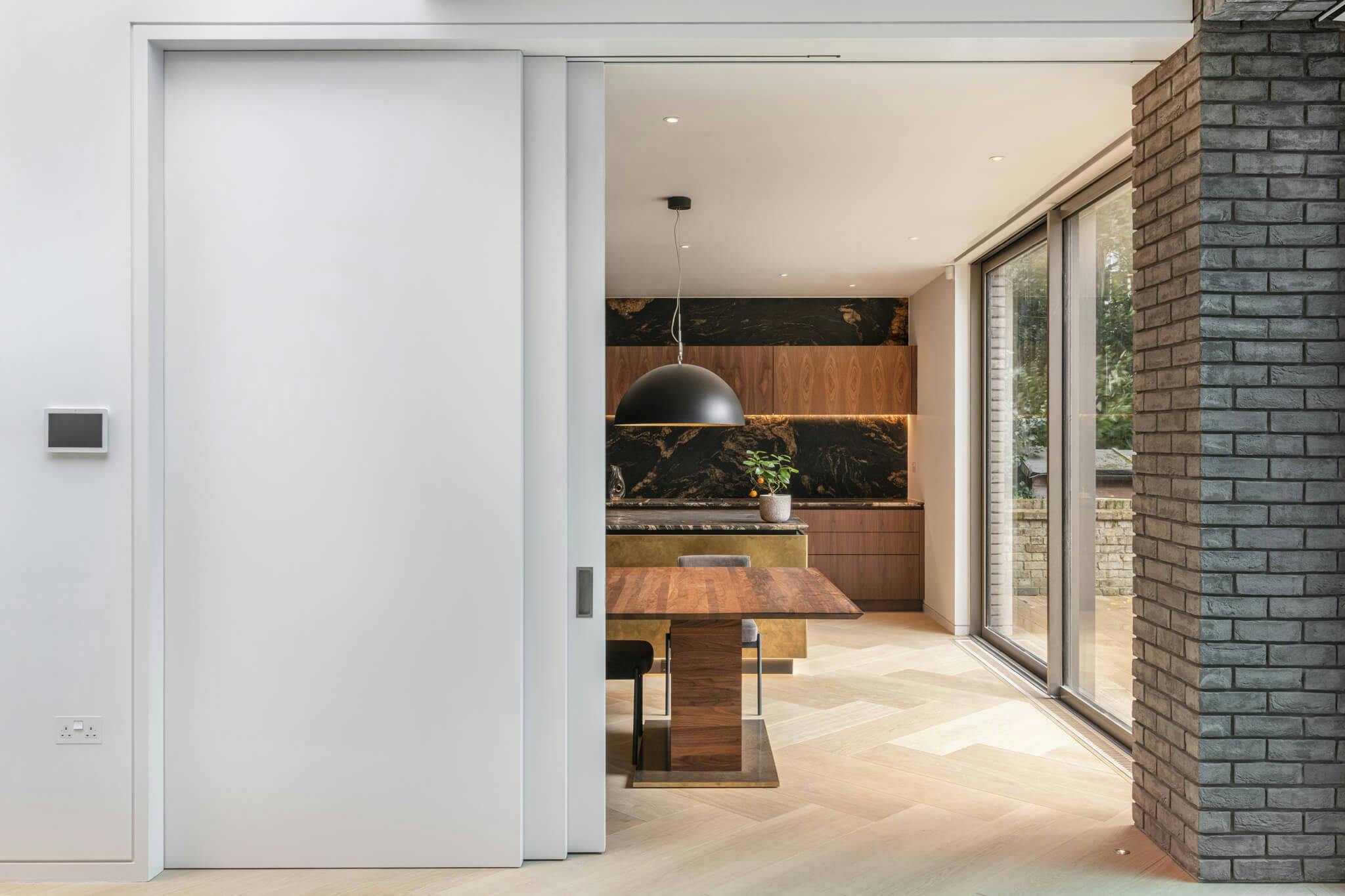 A large set of partially open white telescopic sliding doors leading into a wood and marble kitchen,.