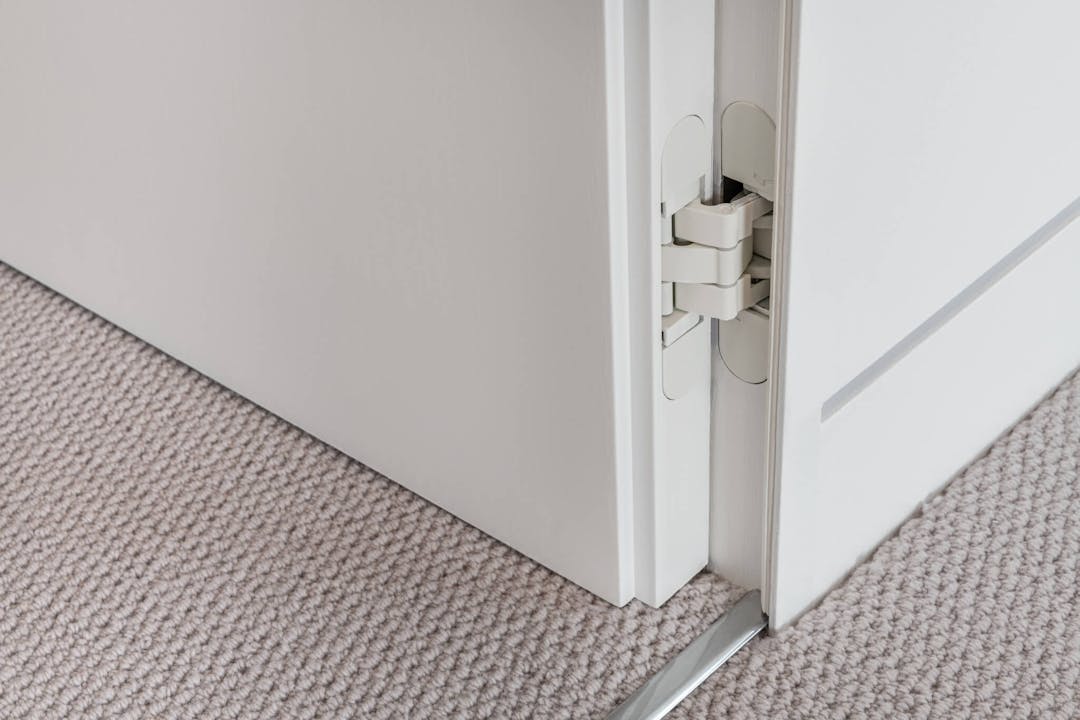Looking down at a carpeted floor and the corner of a white flush door open showing the hinge detail.