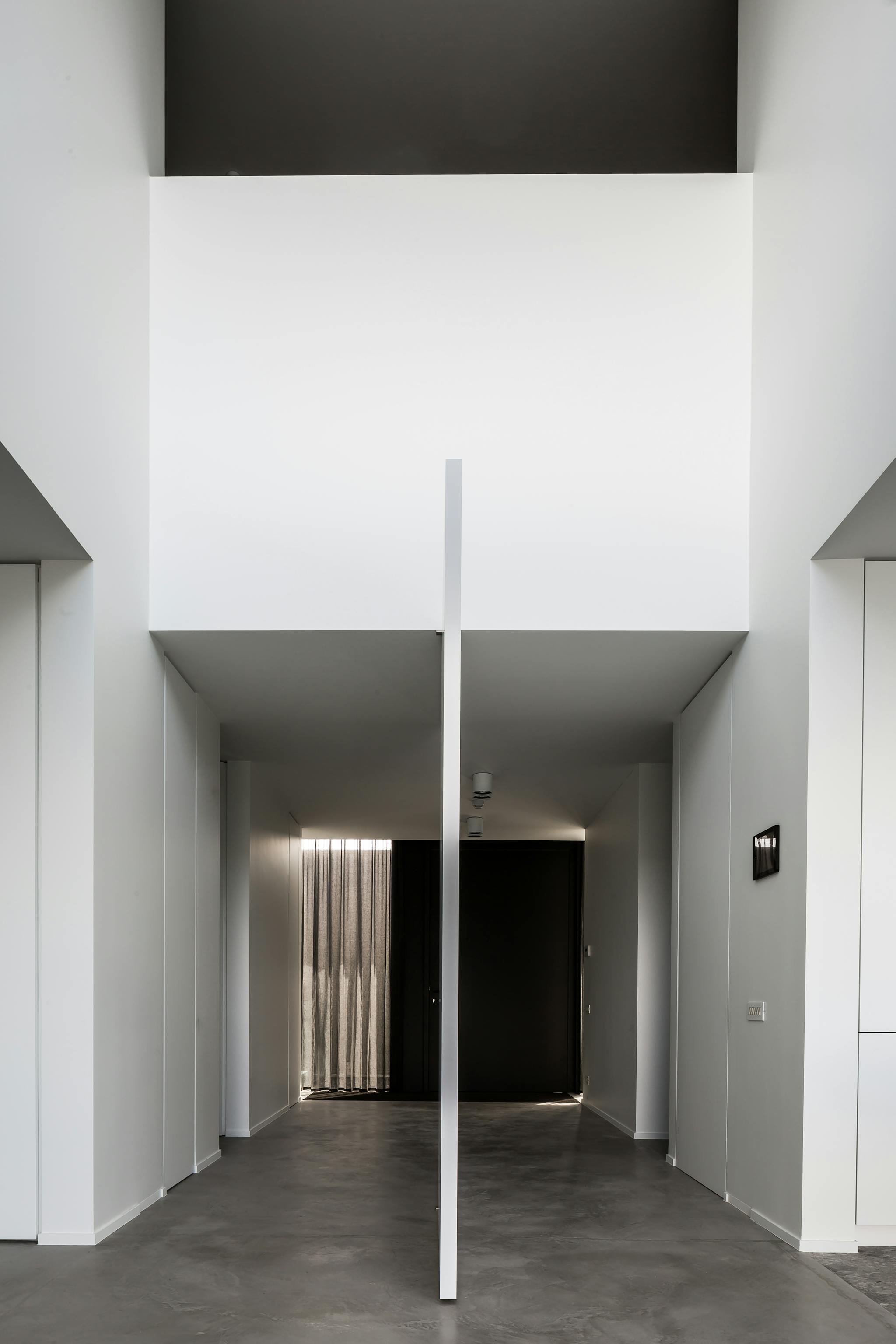 Side profile of a fully open pivoting flush door in a large space with concrete floors and white walls leading towards a dark coloured entrance door.