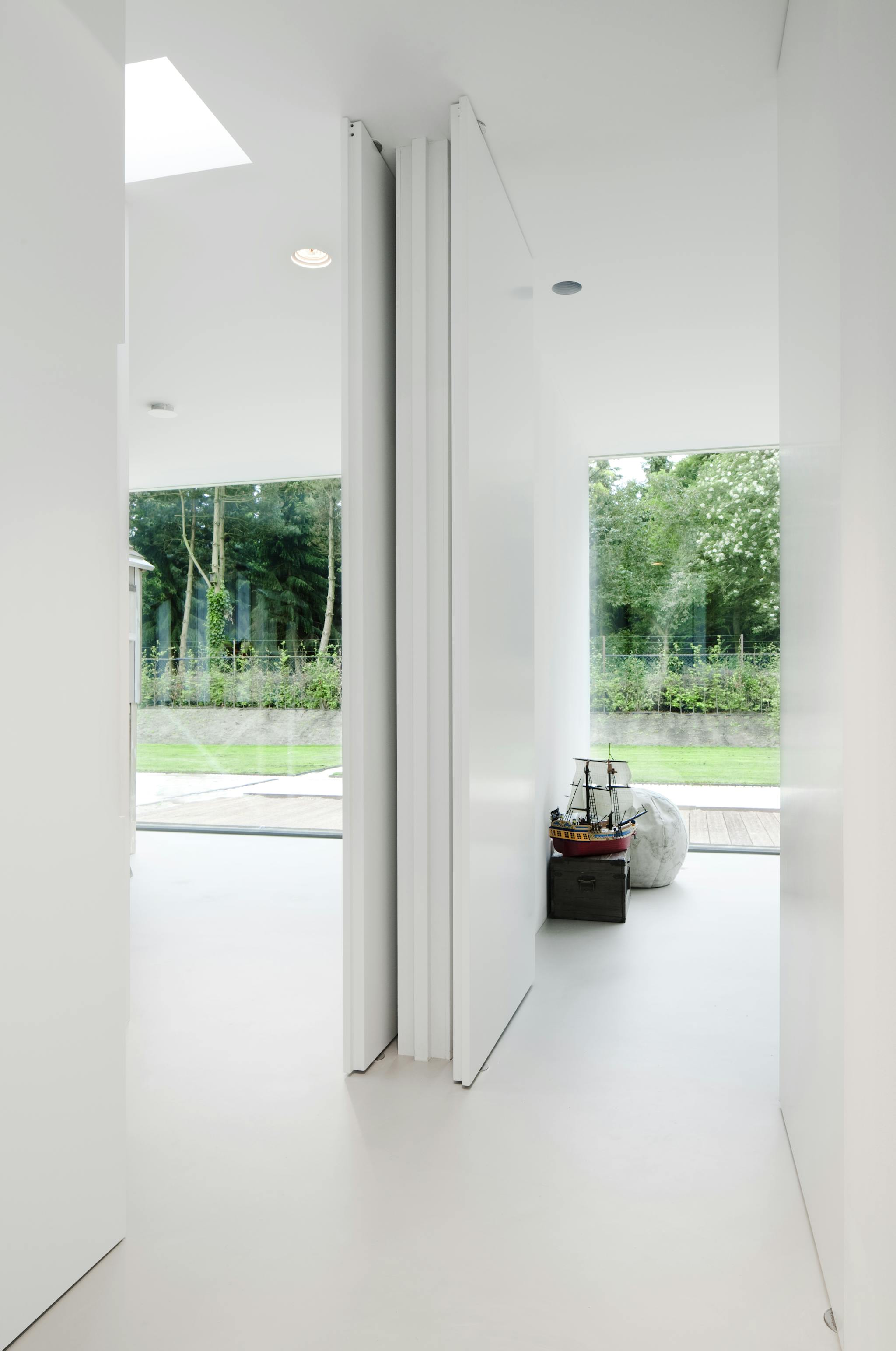 A white minimal interior looking at a dividing wall, looking out into garden through large minimal glazing, with two open pivoting doors