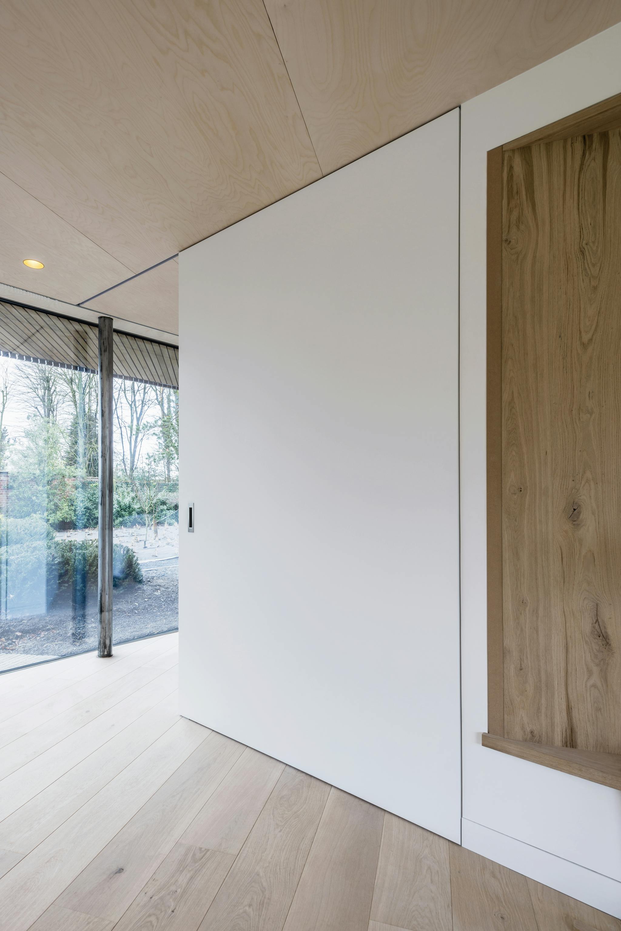 A huge white sliding door in a modern minimal interior with floor to ceiling glazing and wooden floor