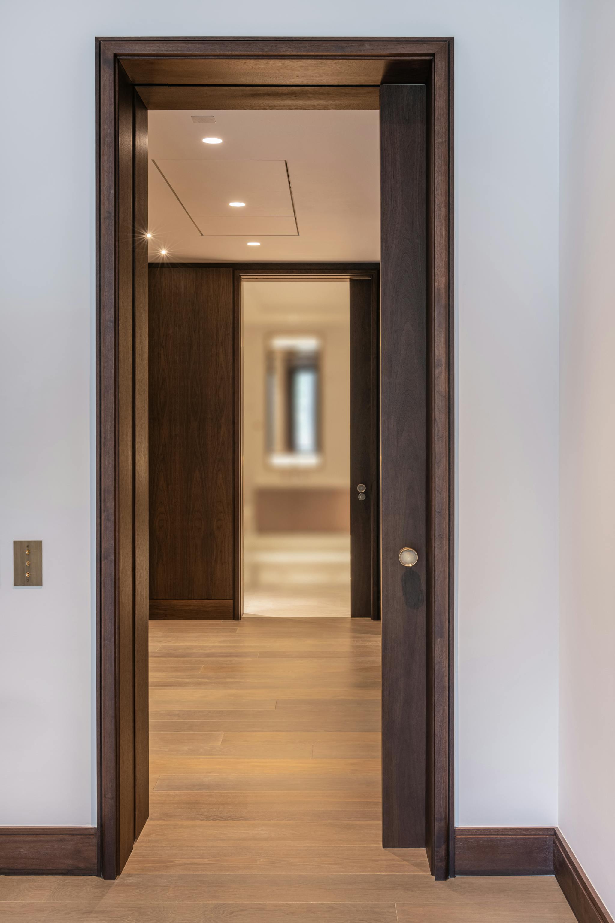 A luxury interior with wooden flooring and a dark heavy set wooden sliding pocket door leading to a hallway reception area
