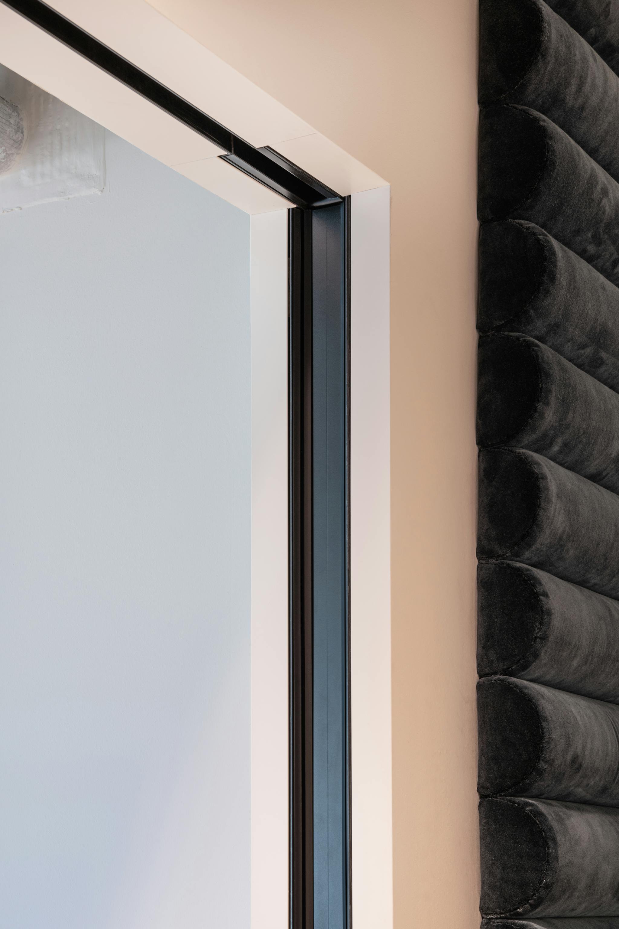 Black track detail of a sliding pocket door in a white wall with dark cushioned wall feature to the right.
