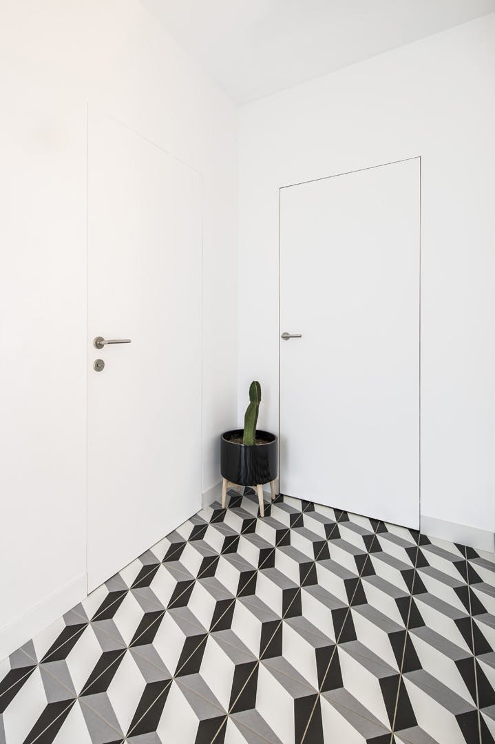 A black, grey and white tiled room with a plant in a black pot with two white invisible flush doors with silver lever handles.