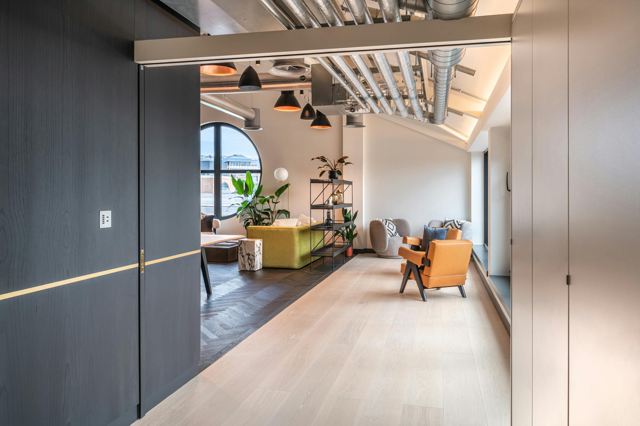 A fully open sliding door recessed into a dark wood wall in a contemporary office corridor leading to a lounge area.