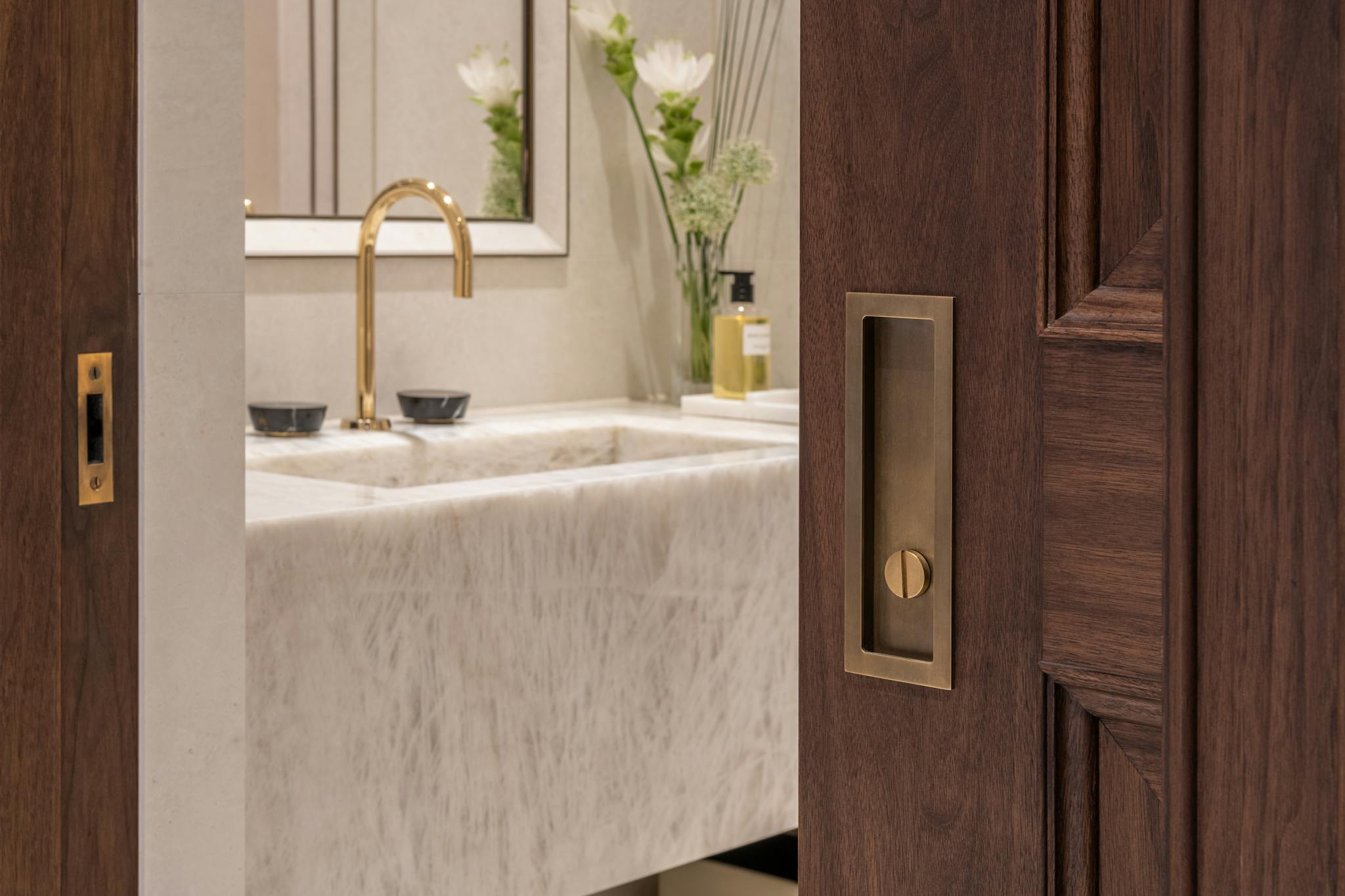 Looking into a luxury marbled bathroom with gold tap from partially closed dark wood sliding pocket door.