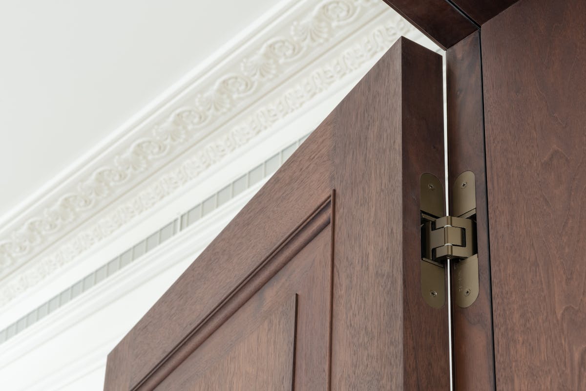 Flush door hinge detail of a dark wood thick set door with traditional white coving in the background.